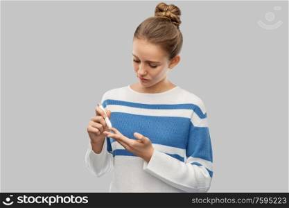 health, medicine and people concept - teenage girl making blood sugar test by glucometer over grey background. teenage girl making blood sugar test by glucometer