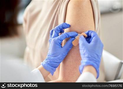health, medicine and vaccination concept - close up of doctor attatching adhesive medical plaster or patch to patient at hospital. close up of doctor attaching patch to patient