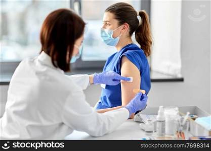 health, medicine and vaccination concept - female doctor wearing protective medical mask and gloves attaching adhesive wound plaster or patch to medical worker at hospital. female doctor attaching patch to medical worker