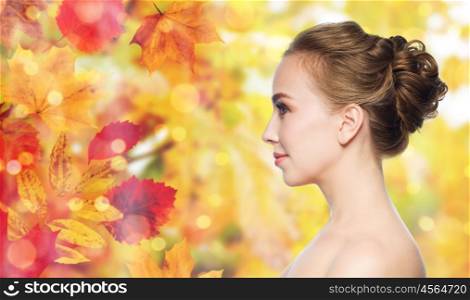 health, people and beauty concept - beautiful young woman face over natural autumn leaves and lights background