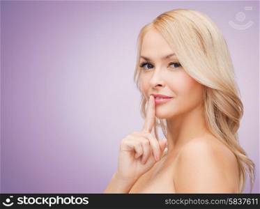 health, people and beauty concept - beautiful young woman holding finger on her lips over violet background