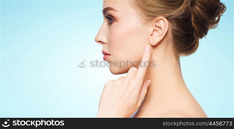 health, people and beauty concept - beautiful young woman pointing finger to her ear over blue background