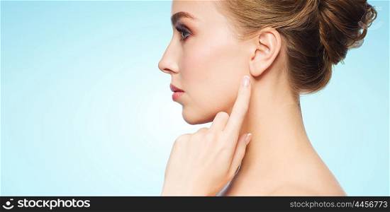 health, people and beauty concept - beautiful young woman pointing finger to her ear over blue background
