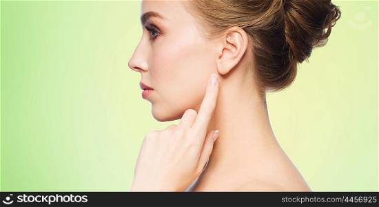 health, people and beauty concept - beautiful young woman pointing finger to her ear over green natural background