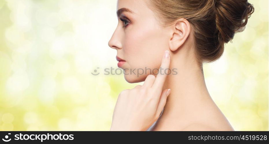 health, people and beauty concept - beautiful young woman pointing finger to her ear over yellow holidays lights background