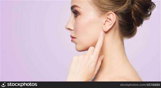 health, people and beauty concept - beautiful young woman pointing finger to her ear over violet background