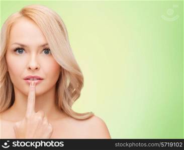 health, people and beauty concept - beautiful young woman touching her lips over green background