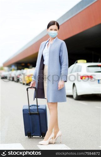 health, people and tourism concept - happy young woman wearing protective medical mask for protection from virus with travel bag on city street. woman with travel bag in protective mask in city