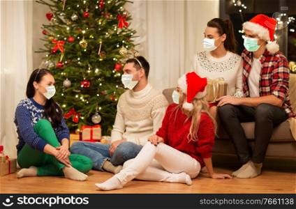 health, people and winter holidays concept - friends wearing face protective medical mask for protection from virus disease with glasses celebrating christmas at home party. friends in masks celebrating christmas at home