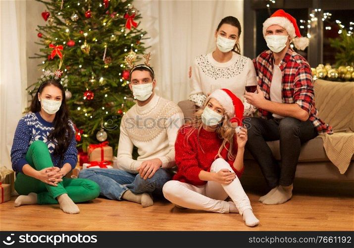health, people and winter holidays concept - friends wearing face protective medical mask for protection from virus disease drinking red wine at home on christmas. friends in masks drinking wine on christmas