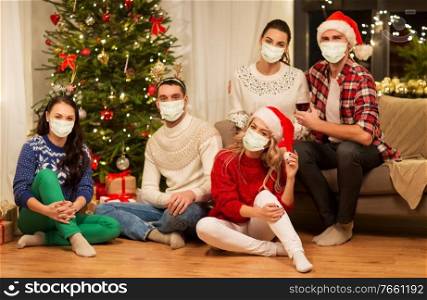 health, people and winter holidays concept - friends wearing face protective medical mask for protection from virus disease drinking red wine at home on christmas. friends in masks drinking wine on christmas