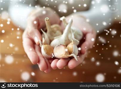 health, people, food, traditional medicine and ethnoscience concept - woman hands holding garlic for cooking or healing over snow. woman hands holding garlic