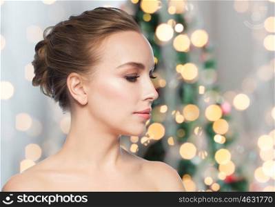 health, people, holidays and beauty concept - beautiful young woman face over christmas tree lights background