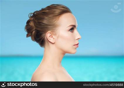 health, people, plastic surgery and beauty concept - beautiful young woman face over blue sea and sky background