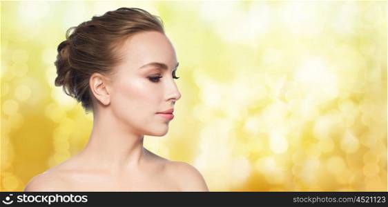 health, people, plastic surgery and beauty concept - beautiful young woman face over yellow holidays lights background