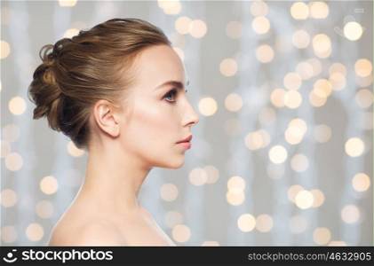 health, people, plastic surgery and beauty concept - beautiful young woman face profile over holidays lights background