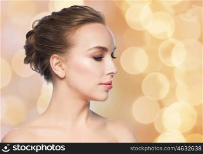health, people, plastic surgery and beauty concept - beautiful young woman face over holidays lights background