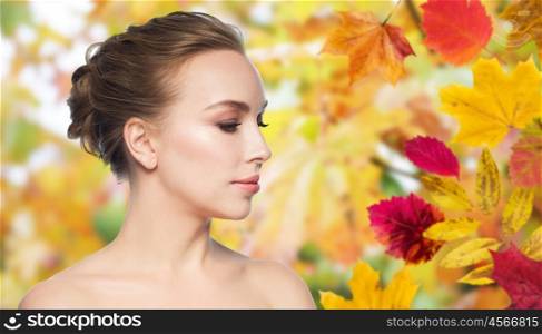 health, people, season and beauty concept - beautiful young woman face over autumn leaves background