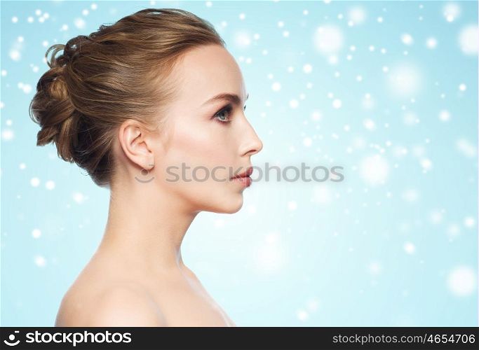 health, people, winter and beauty concept - beautiful young woman face over blue background and snow