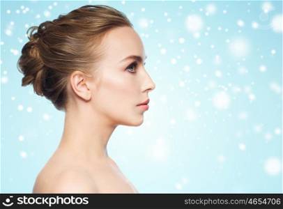 health, people, winter and beauty concept - beautiful young woman face over blue background and snow