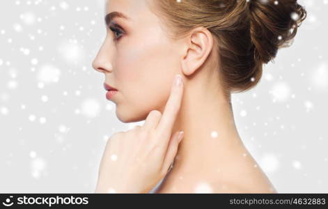 health, people, winter and beauty concept - close up of beautiful young woman pointing finger to her ear over gray background and snow