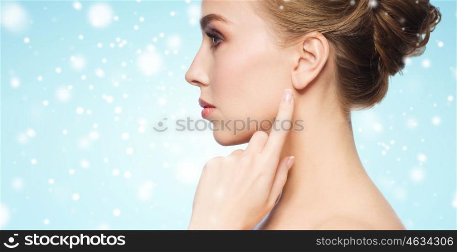 health, people, winter and beauty concept - close up of beautiful young woman pointing finger to her ear over blue background and snow
