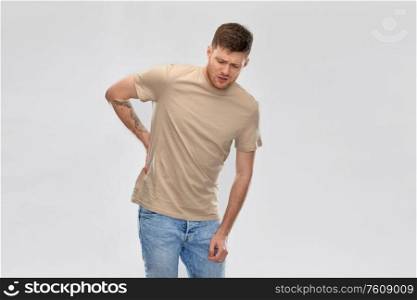 health problem and people concept - unhappy young man suffering from pain in back or reins over grey background. young man suffering from backache