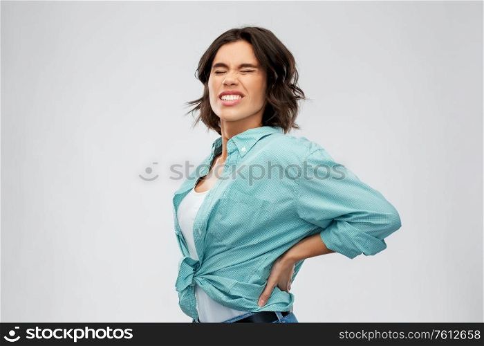 health problem and people concept - unhappy young woman suffering from pain in back or reins over grey background. young woman suffering from backache