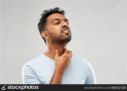 health problem and people concept - unhealthy indian man suffering from neck pain or sore throat over grey background. indian man suffering from neck pain or sore throat