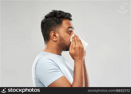 health problem, rhinitis and allergy concept - unhealthy indian man with paper napkin blowing nose over grey background. indian man with paper napkin blowing nose