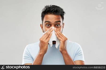 health problem, rhinitis and allergy concept - unhealthy indian man with paper napkin blowing nose over grey background. indian man with paper napkin blowing nose