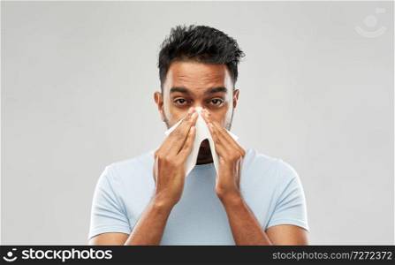 health problem, rhinitis and allergy concept - unhealthy indian man with paper napkin blowing nose over grey background. indian man with paper napkin blowing nose