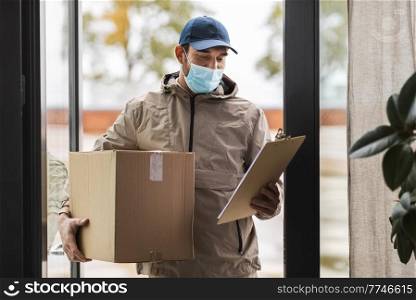 health protection, mail service and pandemic concept - delivery man in face protective mask holding parcel box with clipboard at open door. delivery man in face mask holding parcel box