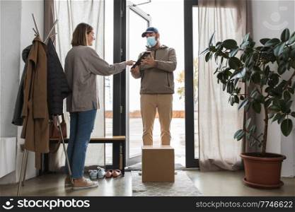 health protection, mail service and pandemic concept - delivery man in face protective mask with parcel box and tablet pc computer and female customer at home. delivery man in mask with tablet pc and woman