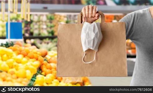 health protection, safe shopping and pandemic concept - close up of woman with paper bag and face protective medical mask over grocery store or supermarket on background. woman with shopping bag and mask at grocery