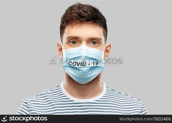 health protection, safety and coronavirus epidemy concept - young man in face protective medical mask with covid-19 word over grey background. young man in face protective medical mask