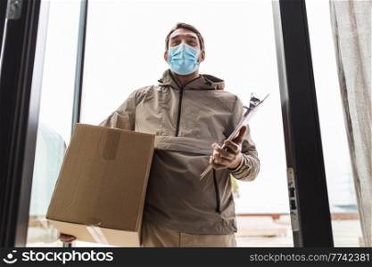 health protection, safety and pandemic concept - delivery man in face protective mask holding parcel box with clipboard at open door. delivery man in mask with parcel box and clipboard