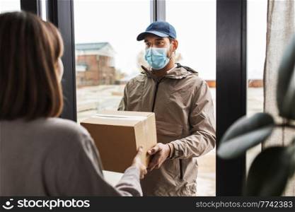 health protection, safety and pandemic concept - delivery man in face protective mask giving parcel box to female customer at home. delivery man in mask giving parcel to customer