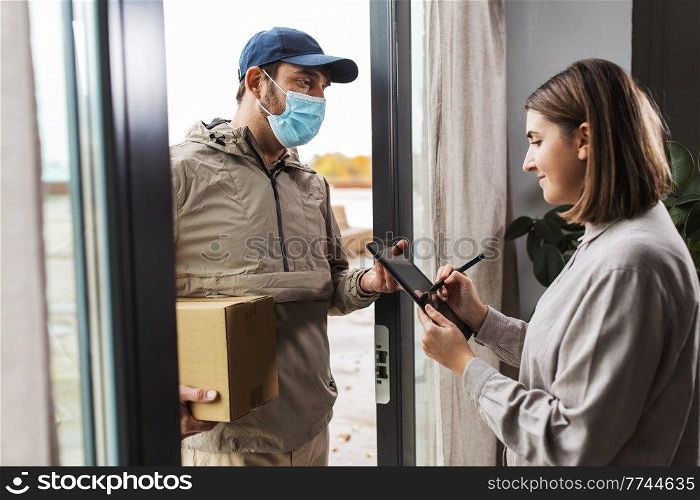 health protection, safety and pandemic concept - delivery man in face protective mask with parcel box and female customer signing digital form on tablet pc computer at home. deliveryman in mask and woman signing digital form