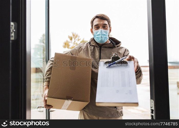health protection, safety and pandemic concept - delivery man in face protective mask holding parcel box with clipboard at open door. delivery man in mask with parcel box and clipboard