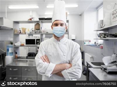 health protection, safety and pandemic concept - male chef cook wearing face protective medical mask over restaurant kitchen background. male chef with in face mask at restaurant kitchen