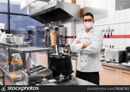 health protection, safety and pandemic concept - male chef cook wearing face protective medical mask over kebab shop kitchen background. male chef with in face mask at kebab shop kitchen