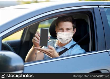 health protection, safety and pandemic concept - man or car driver wearing face protective medical mask showing smartphone. male car driver with smartphone wearing face mask
