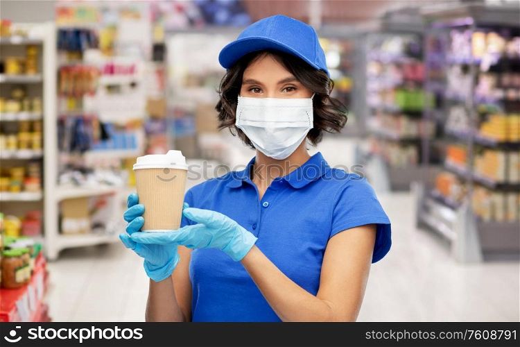health protection, safety and pandemic concept - saleswoman in face protective medical mask and gloves holding disposable takeaway coffee cup over supermarket or grocery store background. saleswoman in mask with coffee cup at store