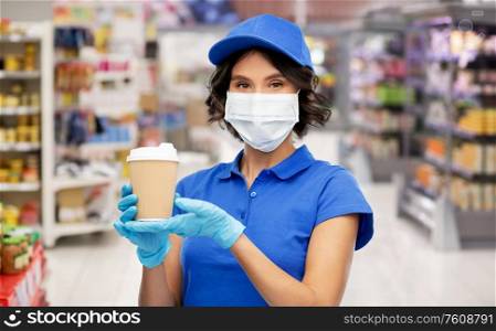 health protection, safety and pandemic concept - saleswoman in face protective medical mask and gloves holding disposable takeaway coffee cup over supermarket or grocery store background. saleswoman in mask with coffee cup at store