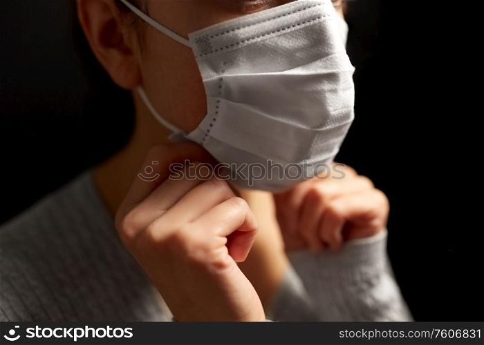 health protection, safety and pandemic concept - sick young woman adjusting protective medical face mask over black background. sick woman adjusting protective medical face mask