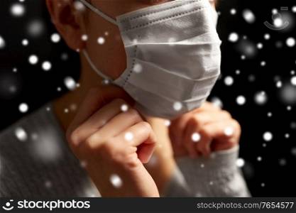 health protection, safety and pandemic concept - sick young woman adjusting protective medical face mask over snow on black background in winter. sick woman adjusting protective medical face mask