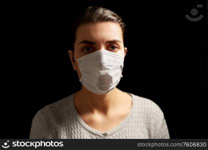 health protection, safety and pandemic concept - sick young woman in protective medical face mask over black background. sick young woman in protective medical face mask