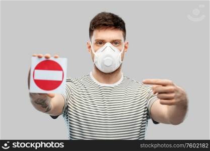 health protection, safety and pandemic concept - young man in protective mask or respirator with valve showing stop sign over grey background. man in respirator mask showing stop sign