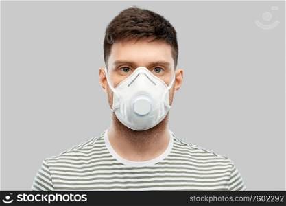 health protection, safety and pandemic concept - young man in protective mask or respirator with valve over grey background. man in protective medical mask or respirator